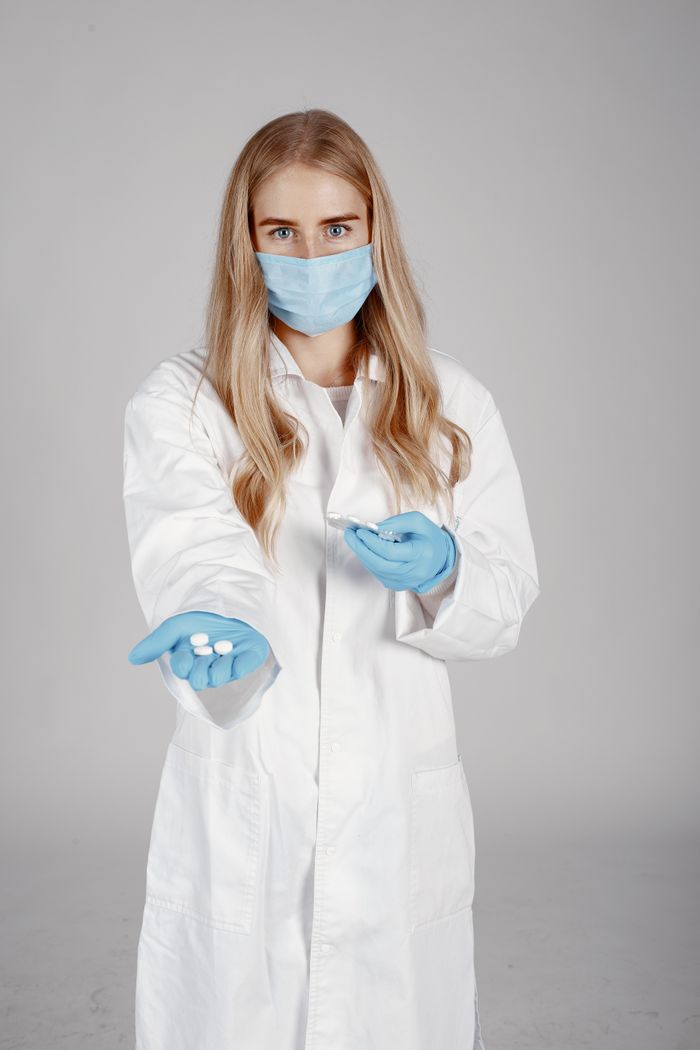 Medical professional in protective gear holding pills for patient care.