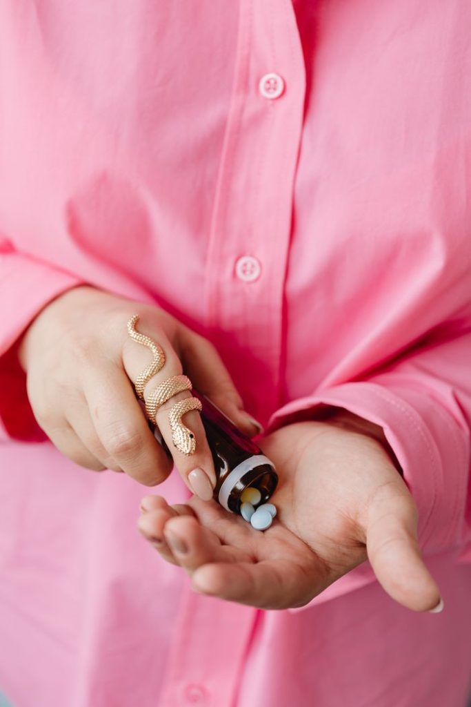 Person in pink shirt pouring pills from brown bottle into hand, showcasing health concept.