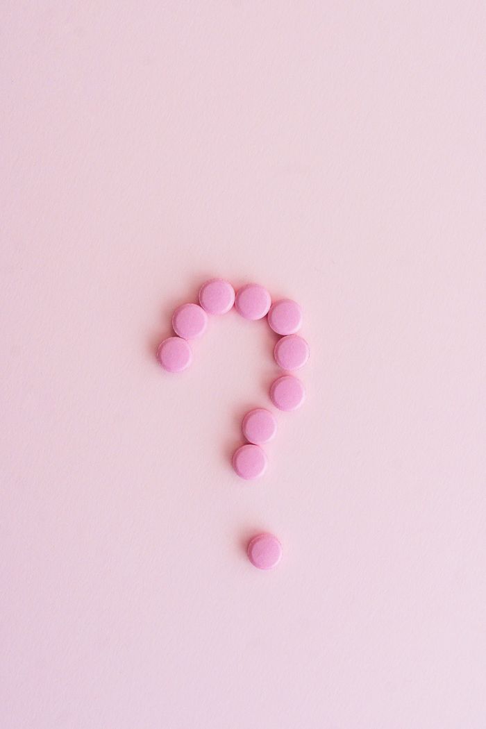 Pink pills forming a question mark on a pastel surface, symbolizing uncertainty in health decisions.